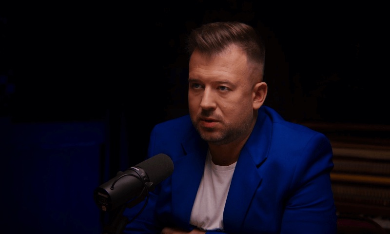 Rozmówca w granatowej marynarce i białej koszulce przed mikrofonem